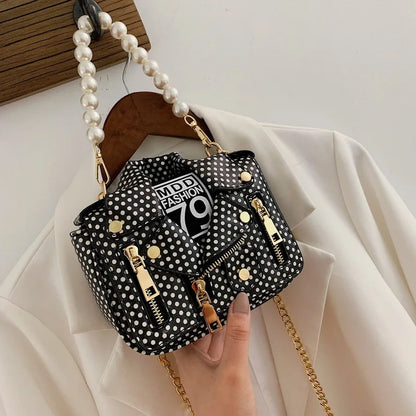 Black polka dot handbag with gold accents and pearl strap on a white background