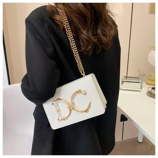 Person holding a white Dolce_CaRaUaN handbag with gold lettering in an indoor setting