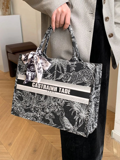 Person holding a black and white patterned tote bag with 'CASTRAINH TADE' branding.